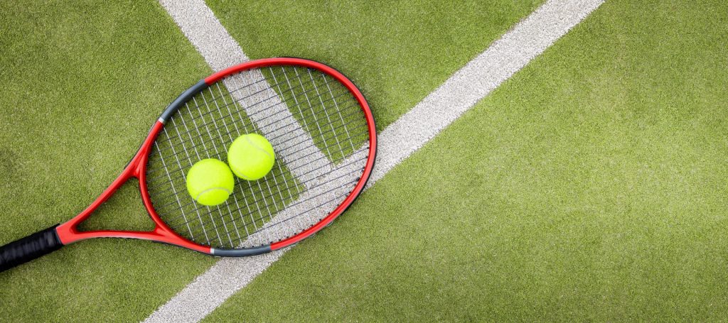Tennis racket with 2 tennis balls sitting on artificial grass