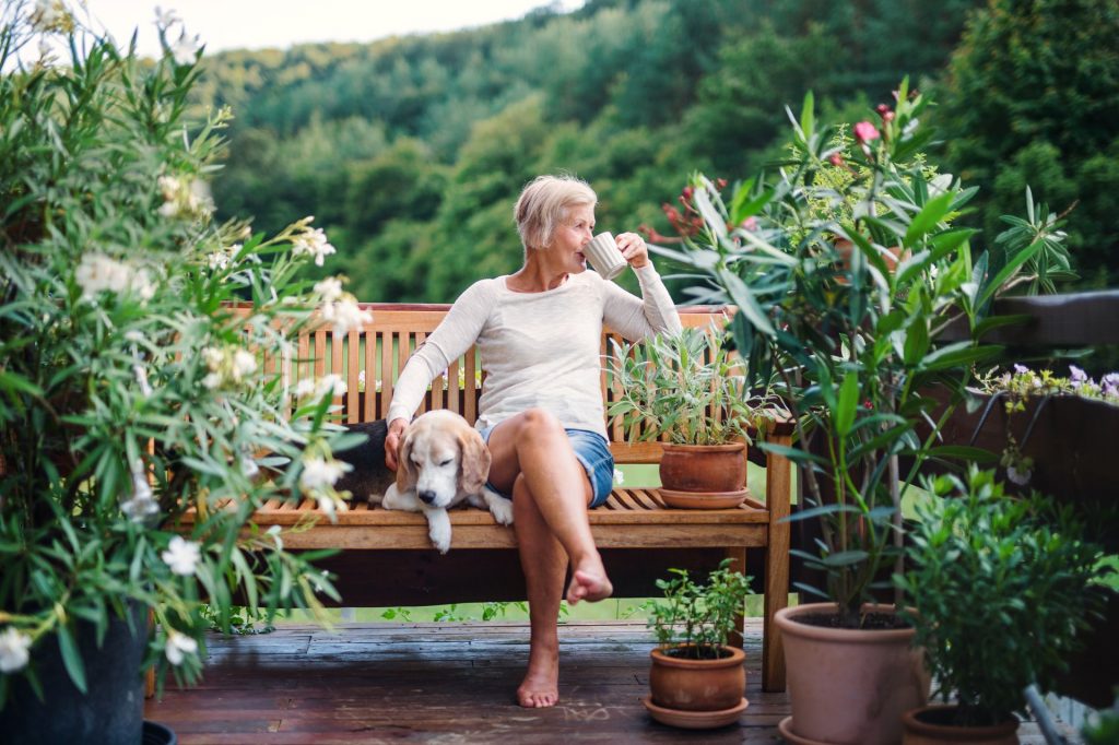 Woman drinking from a cup and relaxing with her dog on a bench in the garden