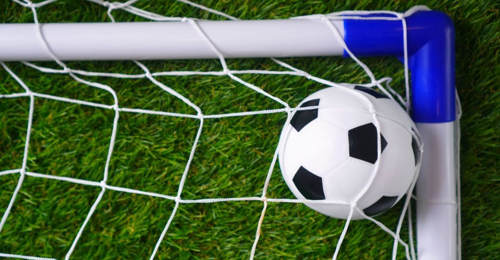 Football and goal net on artificial grass